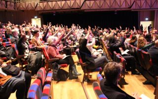 Picture of the March 2024 City Gathering crowd at the Bristol Beacon, some of the crowd have their arms raised.